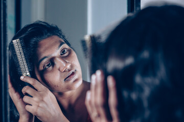 lady combing her hair with hairbrush at mirror.