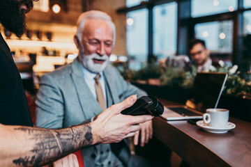 Mature businessman paying with contactless credit card with NFC technology.