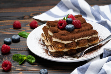 portion of Classic tiramisu dessert with raspberries and blueberries on wooden background