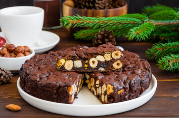 Panforte. Traditional Italian Christmas dessert with nuts and dried fruit on a white plate on a dark wooden background. Horizontal, copy space.