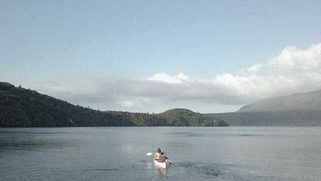 Static shot of couple paddling away in kayak by hilly islands in NZ