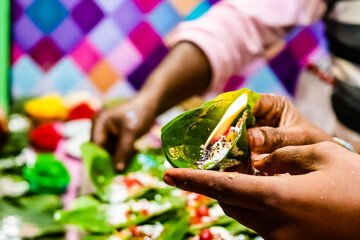hand of a seller holding fire paan, betel leaf on flame.