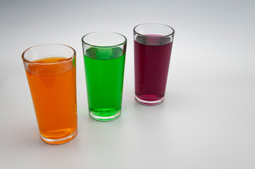 three glasses with different juices on a white background