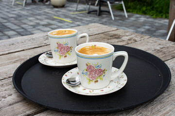 
Two cappuccinos in vintage style cups with rose decoration on a terrace