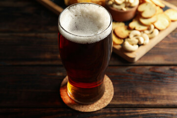 Glass of beer and snacks on wooden table