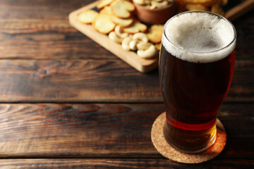 Glass of beer and snacks on wooden table