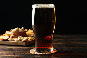 Glass of beer and snacks on wooden table