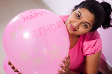 portrait of an indian girl dressed in pink dress with pink balloons on her birthday with selective focus on balloon