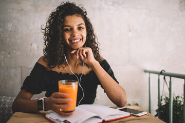 Portrait of cheerful african american 20s woman satisfied with good sound in earphones while having...