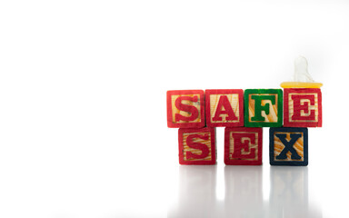 Wood alphabet blocks spell out the words SAFE SEX with a condom sitting on one block. Isolated on white background.