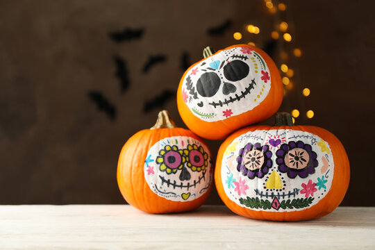 Pumpkins with catrina skull makeup on brown background with blurred lights