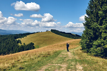 Fototapeta na wymiar Man climbs uphill mountain. Sporty clothes and backpack. Hiking through forest in summer. A path between fir and pine-tree during a sunny day. Dark autumn forest. Local Travel Concept