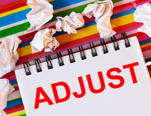 The word ADJUST is written on a white card with a bright striped background. Nearby white crumpled pieces of paper