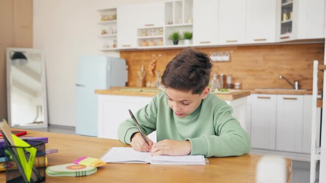 Boy In Kitchen Doing Homework And Chatting with laptop on the table