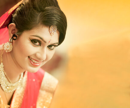 Stunning Indian bride dressed in Hindu red traditional wedding clothes sari embroidered with gold jewelry and a veil smiles tender with extra copy space.