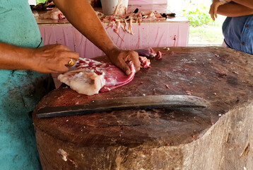 Fatty red meat cut manually on a wooden platform by a butcher with a meat copper knife