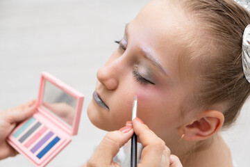 makeup artist makes a festive shining makeup for beautiful young girl. makeup for Halloween or new...