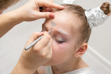 makeup artist makes a festive shining makeup for beautiful young girl. makeup for Halloween or new year.