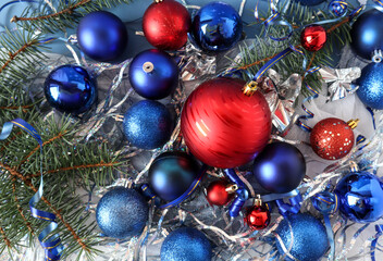 Background of multi-colored Christmas balls of red and blue, tinsel and spruce branches, top view