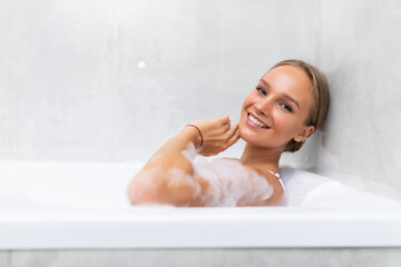 Happy young woman with foam lies in the bathroom and laughs