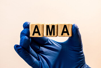The word AMA which is made from wooden cubes. Hands in a blue glove. Isolated on WHITE background.