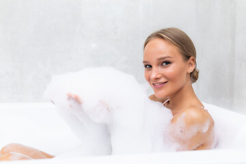 Young woman taking a relaxing bath and blowing on foam