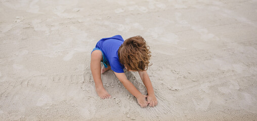 Boy playing on the sand digging holes on the beach at siesta Key florida with the snd and birds 