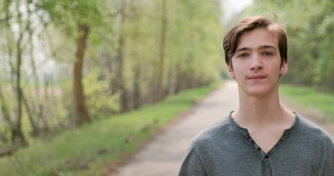 Young man looks on the camera. Teenager outdoors. Closeup face of  handsome guy with sad eyes, on the nature.  Closeup  frustrated teenager face, outside
