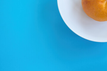 Top view of whole orange grapefruit on white dish on blue background. Diet concept, copy space