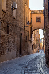 Old Street - Evening view of an old narrow winding cobblestone street, with a brick bridge at above, in Jewish Quarter of the historic city Toledo, Spain.