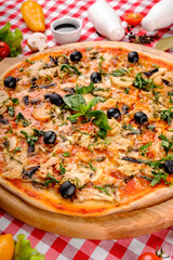 Rustic pizza with chicken meat, cheese, tomato, olive, mushrooms and tomatoes sauce, served on a wooden board for a dinner in italian restaurant background, top view. 