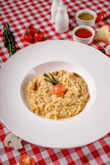 Flat lay. Creamy risotto with cherry tomatoes, rosemary and mushrooms in porcelain plate. Rustic style in italian restaurant background, top view. Italy food. Close up