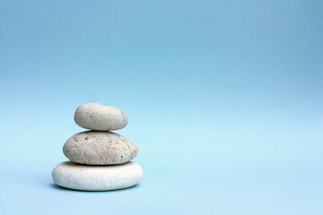 Fototapeta na wymiar Tree grey roundstones on light blue pastel color background. Spa stones, zen like concept.