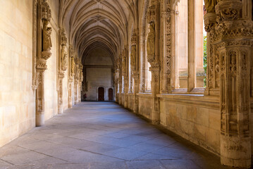 Fototapeta na wymiar Gothic Cloister - A wide-angle view of evening sunlight shining in lower cloister of the 15th-century Isabelline Gothic style church Monastery of Saint John of the Monarchs, Toledo, Spain.