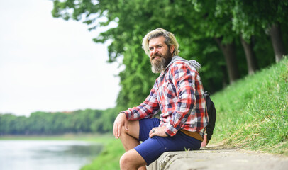 Naklejka na ściany i meble Nice day. Rest and relax. Relaxation and pleasure. Bearded hipster relax outdoors. Man tourist sit riverside. Man with beard and moustache relaxing nature background. Tourism concept. Summer vacation