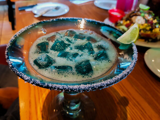 blue coloured soft drink with ice and salt and sugar at edge with lemon