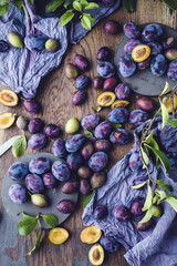 organic purple plums with green leaves on wooden table