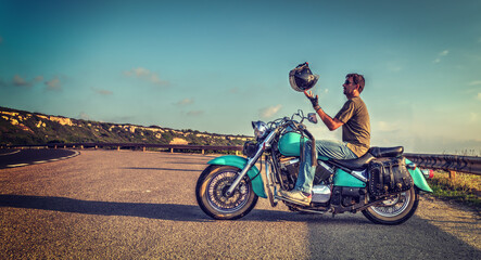 Biker on a classic turquoise motorcycle playing with the helmet