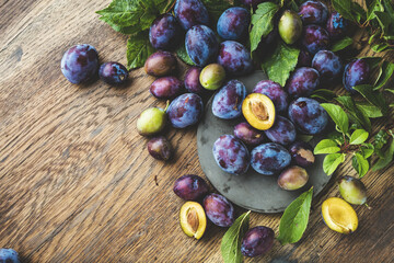 organic purple plums with green leaves on wooden table