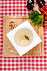 Traditional chicken soup with noodles, vegetables, greens and meat in white plate in restaurant background, top view. Rustic style. Close up.