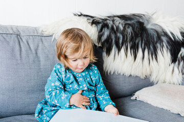 Toddler girl sitting on sofa and reading picture book