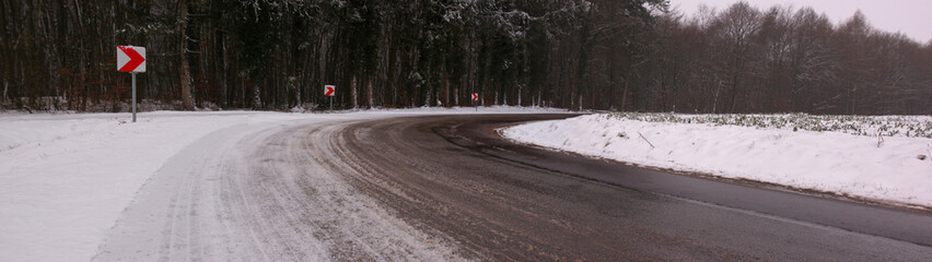 Panoramic view of a dangerous road curve with snow and slush on a cold and overcast winter day in...