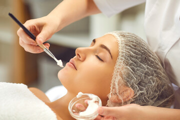 Obraz na płótnie Canvas Hands of dermatologist putting moisturizing cream to womans face during skincare procedure in spa salon