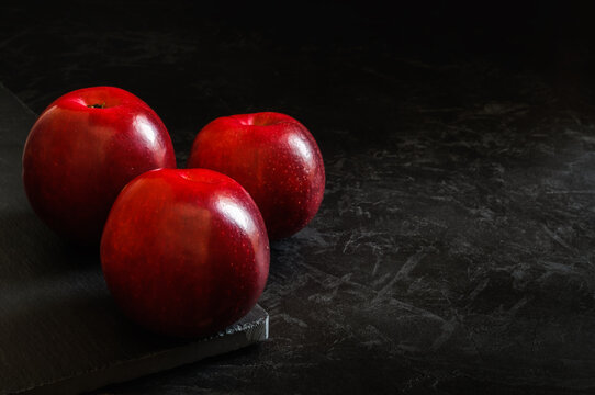 three red ripe apples on a stone board on a black concrete surface. minimalistic dark still life. artistic image with copy space