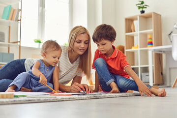 Young mommy and children drawing picture together sitting on floor in nursery