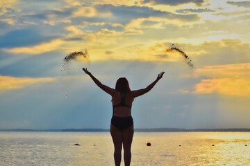 rear view of a woman throwing sand in the air on the beach at sunset