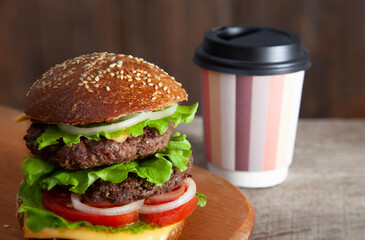 Burger with paper coffee cup to go on wooden tabletop. Close up