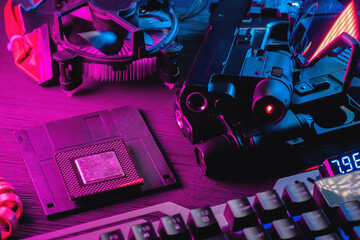 Cyberpunk concept background. Floppy disk, guns, computer keyboard, cpu chip and glasses on the black table background in neon lights.