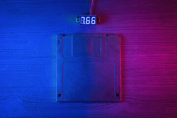 A floppy disk diskette in the neon lights on the black table flat lay background.