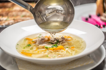 Chicken broth poured from the ladle into a soup in a plate